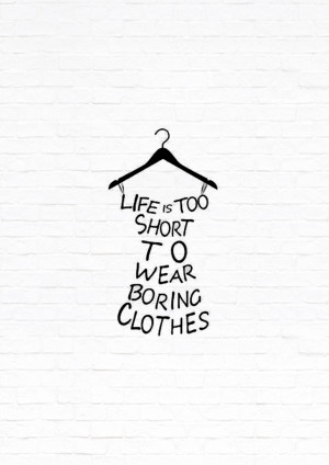 Black hanger with text 'Life is too short to wear boring clothes' on a white brick wall background.
