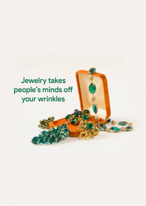 An open orange jewelry box displaying a collection of emerald necklaces, bracelets, and brooches.