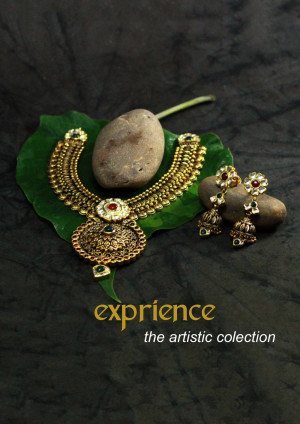 Close-up of a gold necklace and earrings set on a green leaf with stones.