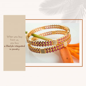 Close-up of two gold bangles adorned with ruby and white stones, resting on a blurred orange flower background.