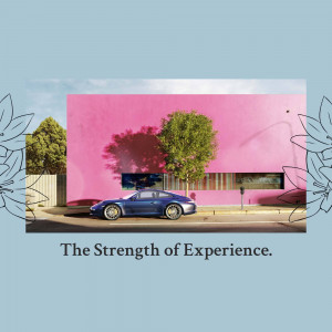 Blue Porsche parked in front of a vibrant pink building with a tree