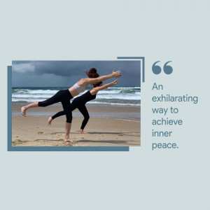 Two women practicing a yoga pose on a beach with a stormy sky in the background.
