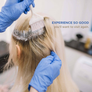 A close-up of a hair stylist applying bleach to a client's hair.