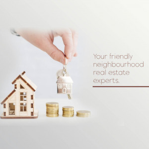 Hand holding a wooden house keychain over a stack of coins, representing real estate investment.