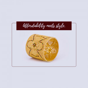 Close-up of a gold-colored bangle with intricate floral detailing on a light background.