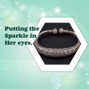 Close-up of a silver bangle with intricate designs, displayed on a black surface within a white hexagon.