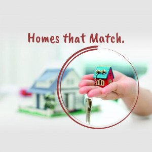 Hand holding a key with miniature houses in the background, representing homeownership.