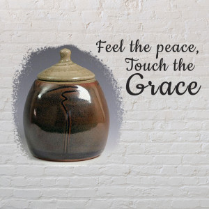 A brown ceramic jar with a lid, set against a white brick wall with the text 'Feel the peace, Touch the Grace'.