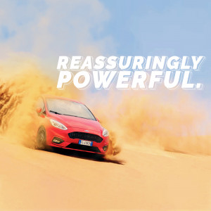 Red Ford Fiesta driving through a sandy desert landscape