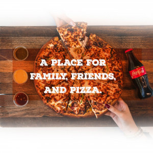 Overhead shot of a pizza being held with drinks and condiments on a wooden table.