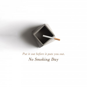 A concrete ashtray with a lit cigarette and text promoting No Smoking Day.