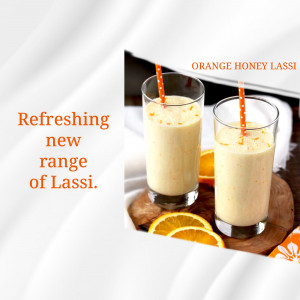 Two glasses of orange honey lassi with orange slices and a wooden coaster.