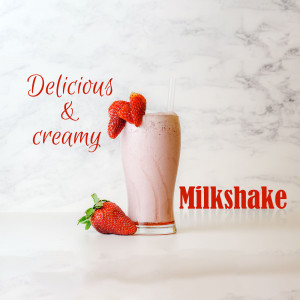 A glass of strawberry milkshake with fresh strawberries, on a marble surface.