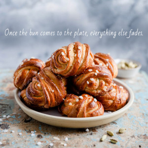 A stack of golden-brown cinnamon buns on a plate with sesame seeds and pistachios.