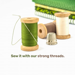 Close-up of green thread spool, brown thread spool, thimble, and stack of fabric