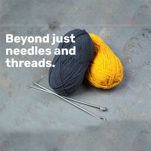 Close-up of gray and yellow yarn balls with knitting needles on a textured surface.