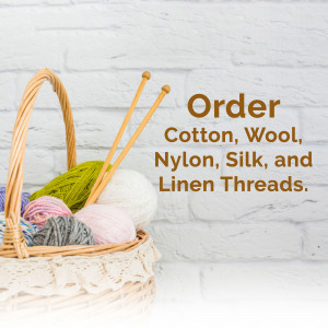 A wicker basket filled with colorful yarn balls and knitting needles against a white brick wall.