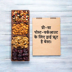 Top-down view of a wooden tray filled with various dry fruits and nuts next to a notepad with text in Hindi.