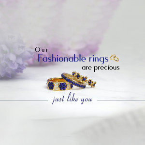 Close-up of gold and blue gemstone rings on a marble surface with lilac flowers.