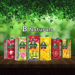 Assortment of B Naturals fruit juice cartons on a wooden surface with green foliage background.