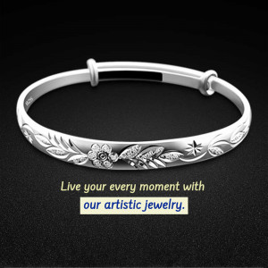 Close-up of a silver bangle bracelet with floral engravings on a black background.