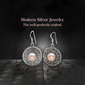 Close-up of silver earrings with pearl accents on a dark wooden surface