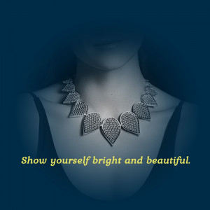 Close-up of a woman wearing a silver, ornate necklace against a dark background.