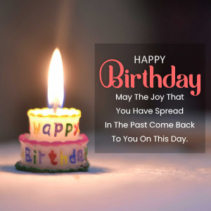 A lit birthday candle on a small cake with 'Happy Birthday' written on it.