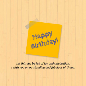 A yellow sticky note with 'Happy Birthday!' written on it, taped to a light brown wooden surface.