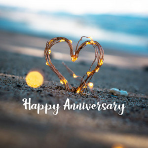 Heart shape made of lights on a beach with 'Happy Anniversary' text