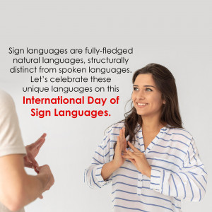 A woman smiling and using sign language with another person partially visible.
