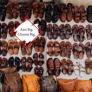 A wall covered in various styles of leather sandals and bags, with a promotional sign.