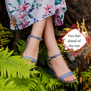 Close-up of a woman's feet wearing blue sandals in a lush green forest setting.
