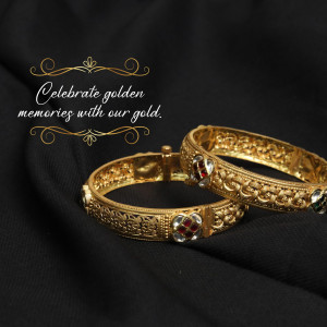 Two ornate gold bangles with red gemstone accents on a black silk background.