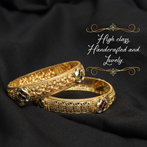Close-up of two ornate gold bangles with gemstone accents on a black background.