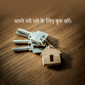 Keys and a wooden house charm on a wooden surface with Hindi text.