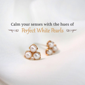 Close-up of delicate gold and pearl earrings on a white silk background.