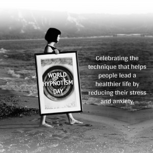 Woman holding a framed World Hypnotism Day poster on a beach.