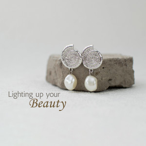 Close-up of silver and pearl drop earrings on a stone surface