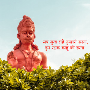 Large red Hanuman statue with text in Hindi and green foliage