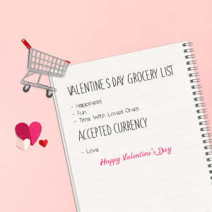 A miniature shopping cart attached to a notebook with a Valentine's Day grocery list and hearts.