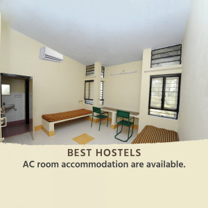 A simple, clean AC room in a hostel with a bed, table, and chairs.