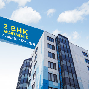 Modern apartment building with a blue banner advertising 2 BHK apartments for rent.