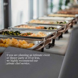 A long line of stainless steel chafing dishes filled with various food items, set up for a buffet.