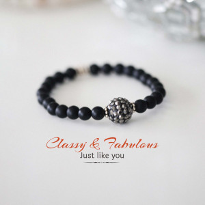 Close-up of a black beaded bracelet with a sparkling silver charm.