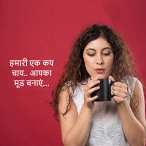 A woman with curly hair holding a black mug of tea and smiling.
