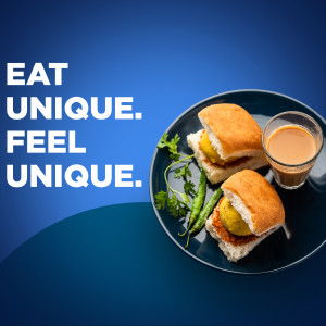 Close-up of Vada Pav with a glass of chai on a blue plate.