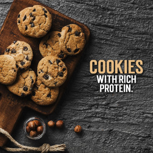 A wooden board filled with chocolate chip cookies and a small bowl of hazelnuts.