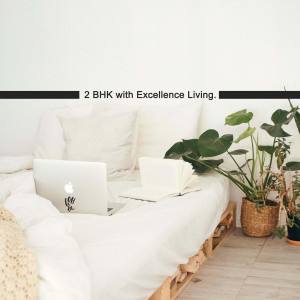 A laptop on a bed with pillows and a plant in a bright room.