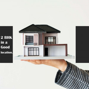 A hand holding a model of a 2 BHK house.